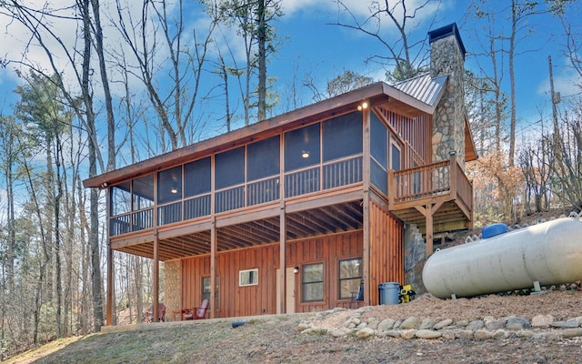 back of property featuring board and batten siding, a sunroom, metal roof, and a chimney