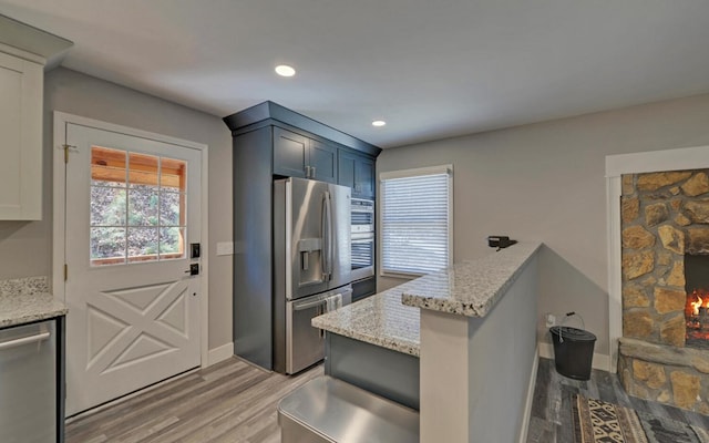 kitchen with baseboards, light wood-style flooring, appliances with stainless steel finishes, light stone counters, and recessed lighting