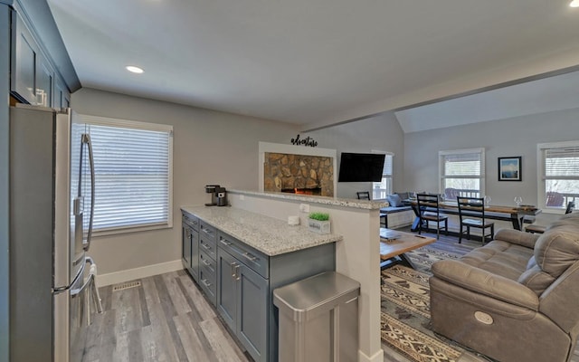 kitchen featuring freestanding refrigerator, open floor plan, vaulted ceiling, light wood-type flooring, and a peninsula