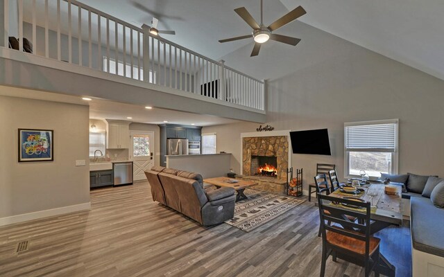 living area with baseboards, light wood-style flooring, ceiling fan, a fireplace, and high vaulted ceiling