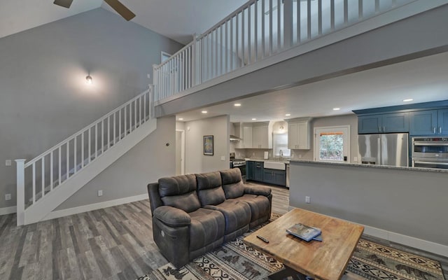 living area with a high ceiling, stairway, wood finished floors, and baseboards