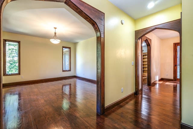 empty room featuring arched walkways, hardwood / wood-style flooring, and baseboards
