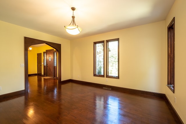 unfurnished room with arched walkways, wood finished floors, and baseboards