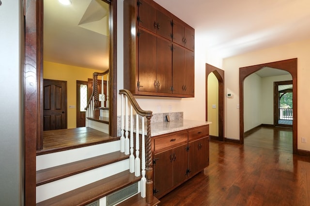 staircase with arched walkways, wood finished floors, and baseboards