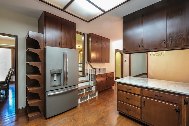 kitchen with stainless steel fridge with ice dispenser, dark wood-style floors, arched walkways, light stone counters, and a chandelier
