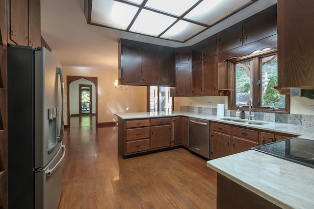 kitchen featuring appliances with stainless steel finishes, a sink, dark wood-style floors, a peninsula, and light countertops