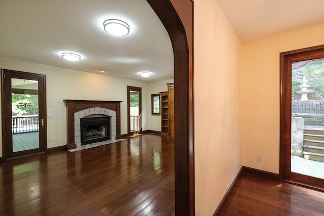 unfurnished living room with dark wood-style flooring, a tile fireplace, baseboards, and arched walkways