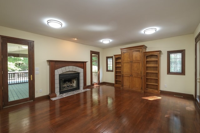unfurnished living room with dark wood-style flooring, healthy amount of natural light, baseboards, and a tile fireplace
