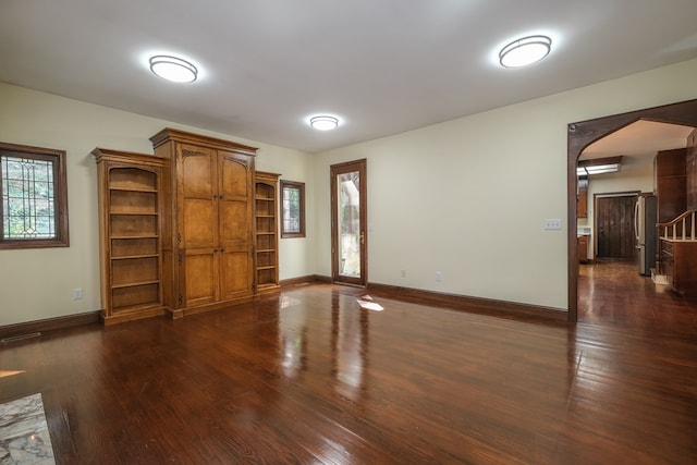 unfurnished living room with arched walkways, dark wood-style flooring, and baseboards