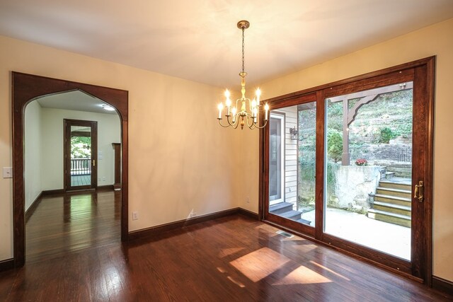 unfurnished dining area with a chandelier, healthy amount of natural light, arched walkways, and dark wood-type flooring