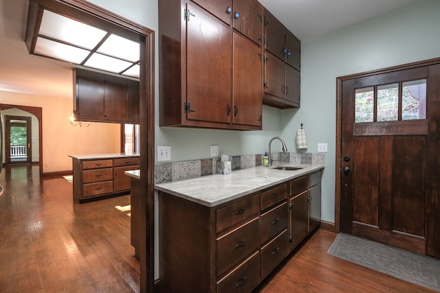 kitchen featuring dark wood-style flooring, a sink, light countertops, arched walkways, and baseboards
