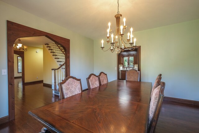 dining room featuring a chandelier, arched walkways, wood finished floors, stairway, and baseboards