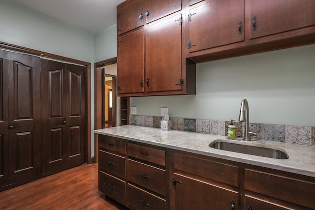 kitchen with a sink, dark wood finished floors, dark brown cabinetry, and light stone countertops