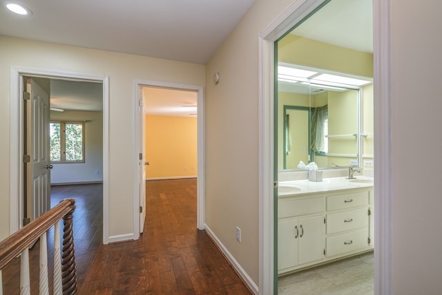 hallway with a sink, wood finished floors, baseboards, and recessed lighting