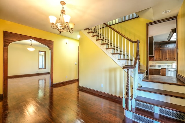 stairs with wood finished floors, arched walkways, a chandelier, and baseboards