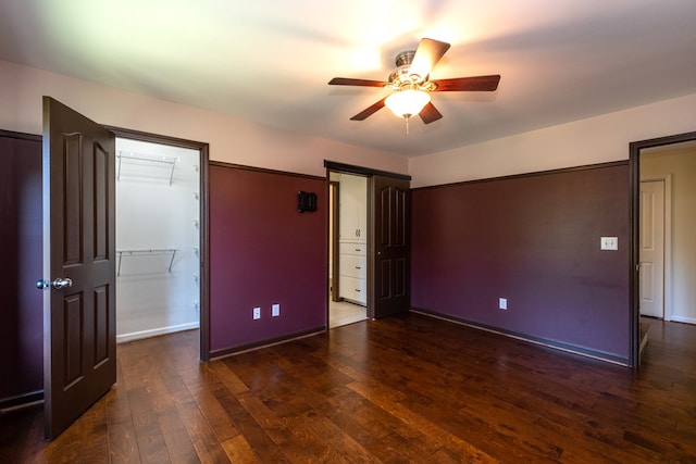 unfurnished bedroom with hardwood / wood-style floors, baseboards, ceiling fan, and a walk in closet