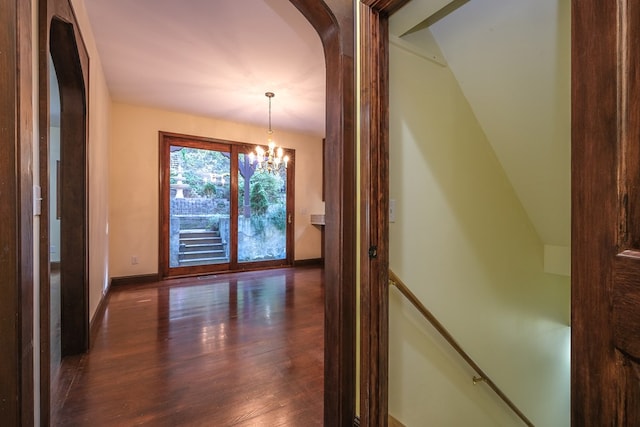 hallway with a chandelier, dark wood-type flooring, arched walkways, baseboards, and an upstairs landing