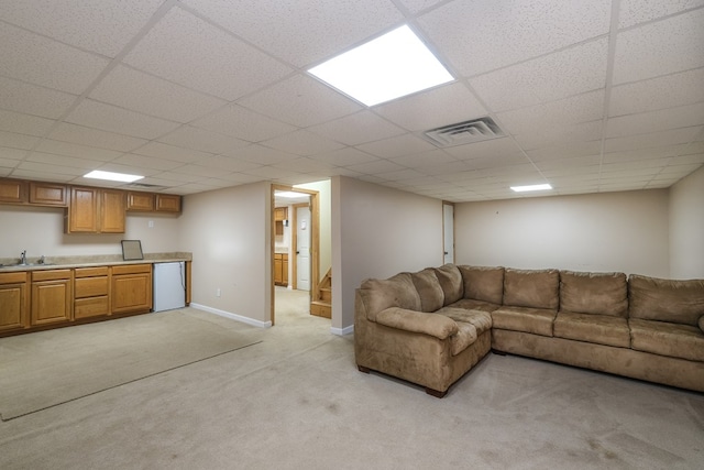 living room featuring light carpet, stairs, a drop ceiling, and baseboards