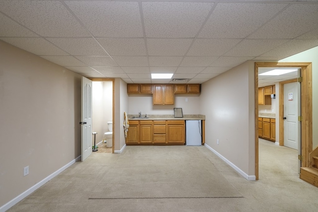 kitchen with fridge, a sink, light carpet, a paneled ceiling, and baseboards