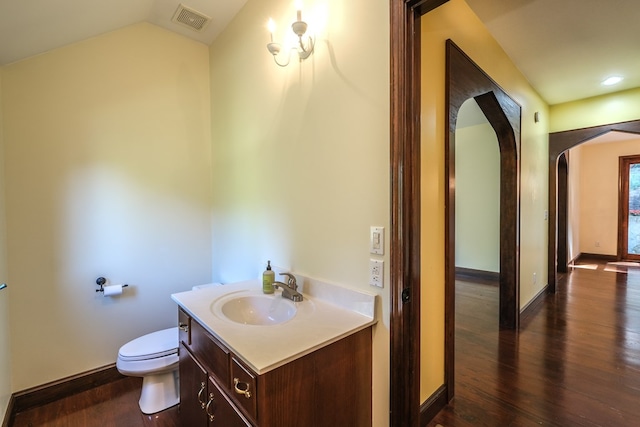 bathroom with vanity, toilet, wood finished floors, baseboards, and lofted ceiling
