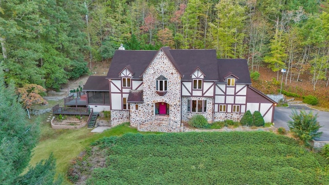english style home featuring a wooded view, stairway, a wooden deck, and asphalt driveway