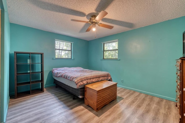 bedroom featuring ceiling fan, baseboards, multiple windows, and wood finished floors