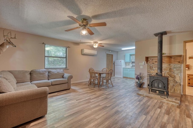 living room with light wood-type flooring, a wood stove, ceiling fan, an AC wall unit, and a textured ceiling