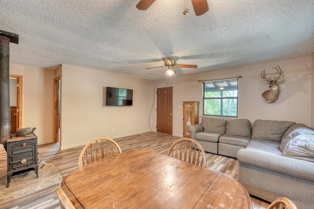 dining area with light wood-type flooring, ceiling fan, and a wood stove