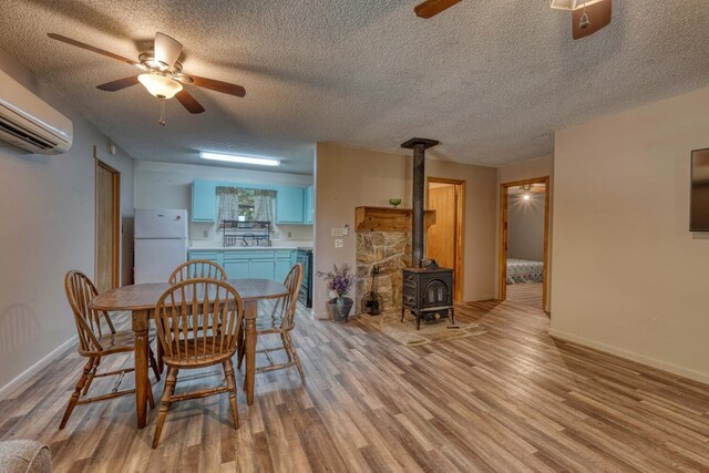 dining space featuring a wall mounted AC, a textured ceiling, a wood stove, ceiling fan, and light hardwood / wood-style floors