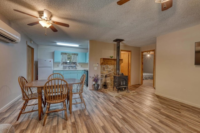 dining area with a ceiling fan, baseboards, a wood stove, a textured ceiling, and light wood-type flooring