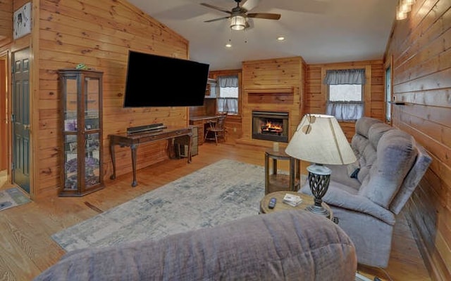 living area with wood finished floors, a ceiling fan, lofted ceiling, a lit fireplace, and wood walls