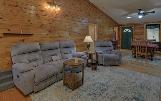 living room featuring a ceiling fan, vaulted ceiling, wood finished floors, and wood walls