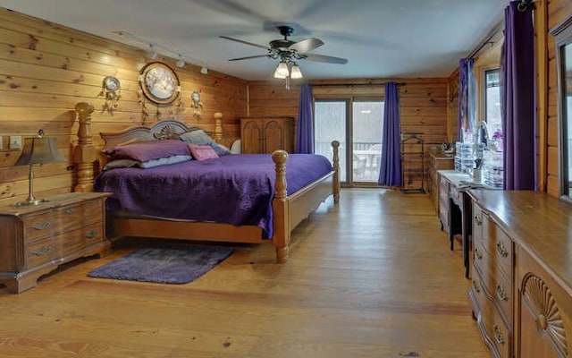 bedroom with access to outside, wood walls, track lighting, and light wood finished floors