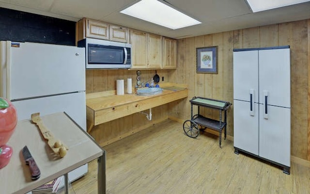 kitchen with wooden walls, light wood-style flooring, freestanding refrigerator, white fridge, and stainless steel microwave