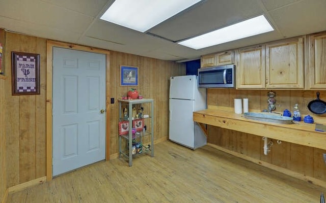 kitchen featuring stainless steel microwave, light wood finished floors, wood walls, and freestanding refrigerator