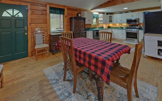 dining area featuring light wood finished floors, wood walls, and vaulted ceiling