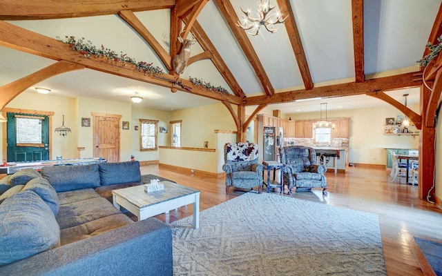 living room with a notable chandelier, light hardwood / wood-style flooring, high vaulted ceiling, and beam ceiling