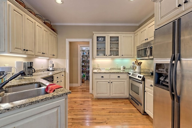 kitchen featuring appliances with stainless steel finishes, sink, light stone counters, ornamental molding, and light hardwood / wood-style flooring