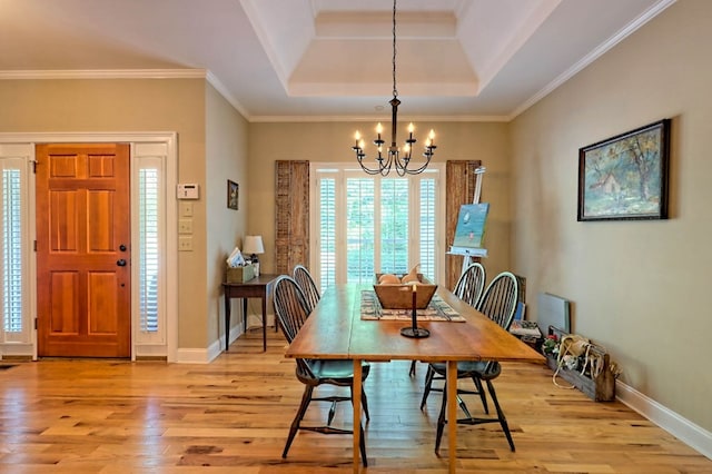 dining room with light hardwood / wood-style floors, ornamental molding, a tray ceiling, and an inviting chandelier