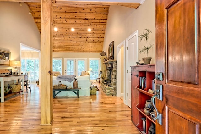 interior space featuring a stone fireplace, light hardwood / wood-style flooring, high vaulted ceiling, and wooden ceiling