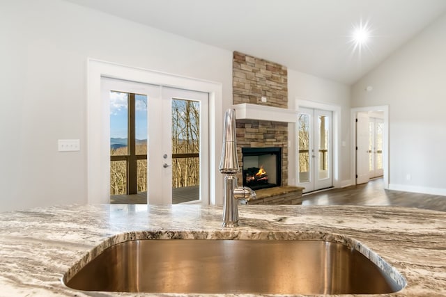 kitchen featuring lofted ceiling, sink, light stone counters, a stone fireplace, and french doors