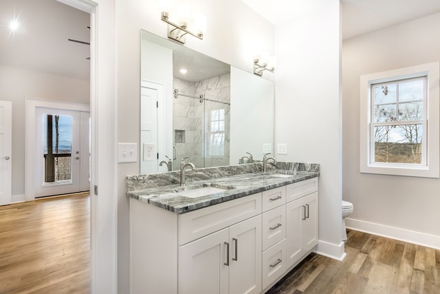 bathroom featuring wood finished floors, a sink, baseboards, double vanity, and a stall shower