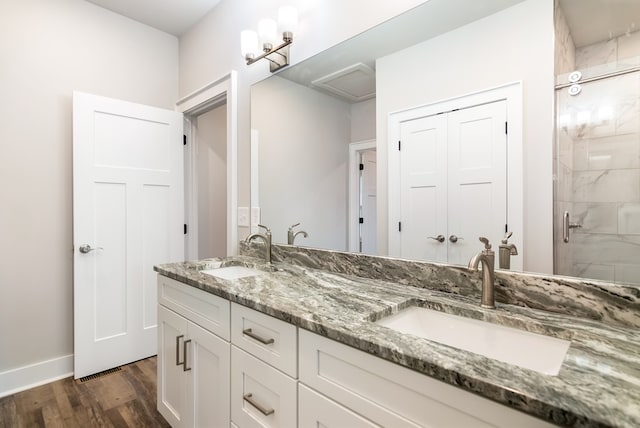 full bathroom with double vanity, tiled shower, a sink, and wood finished floors