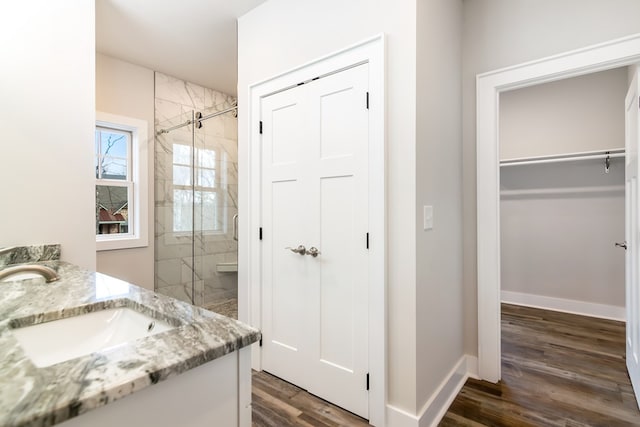 bathroom with a stall shower, baseboards, wood finished floors, a walk in closet, and vanity