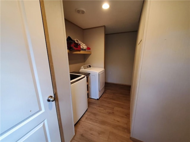 clothes washing area with washing machine and clothes dryer and light wood-type flooring