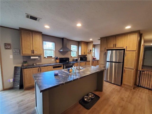 kitchen with wall chimney exhaust hood, sink, black appliances, light hardwood / wood-style floors, and an island with sink