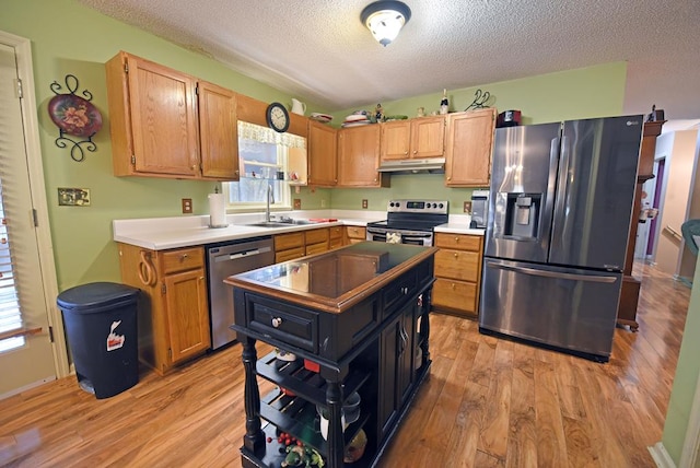 kitchen with light hardwood / wood-style floors, stainless steel appliances, a textured ceiling, and sink