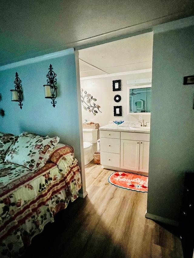 bedroom with crown molding, wood-type flooring, connected bathroom, and sink