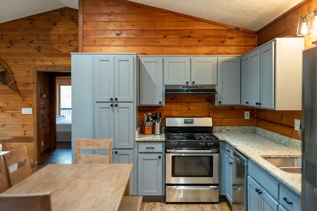 kitchen featuring light stone counters, stainless steel appliances, wood walls, lofted ceiling, and light hardwood / wood-style flooring