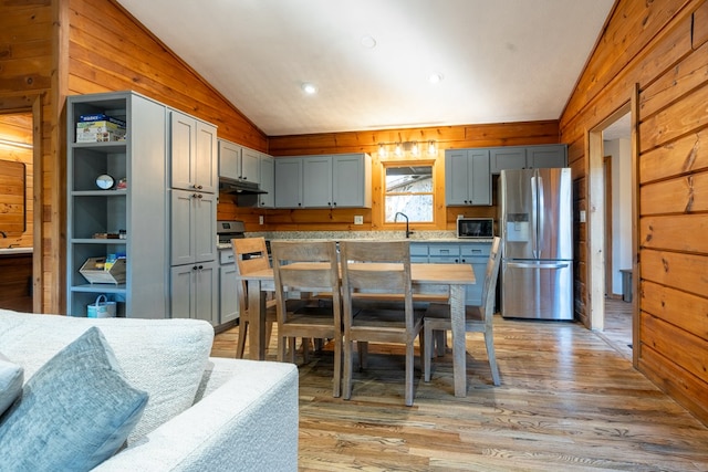 kitchen with wood walls, stainless steel refrigerator with ice dispenser, lofted ceiling, and light hardwood / wood-style flooring